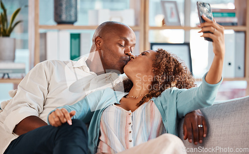 Image of Couple, selfie and kiss on sofa in home living room, bonding or having fun together. Interracial, romantic picture and black man and woman taking photo while kissing for love, memory or social media.