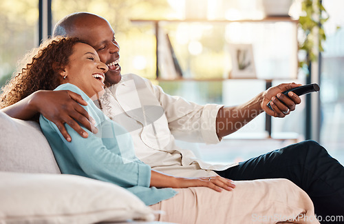 Image of Couple, watching tv and laughing on sofa in home living room, bonding and hug. Interracial, television and funny black man and woman relax on couch streaming comedy movie, film or meme video online