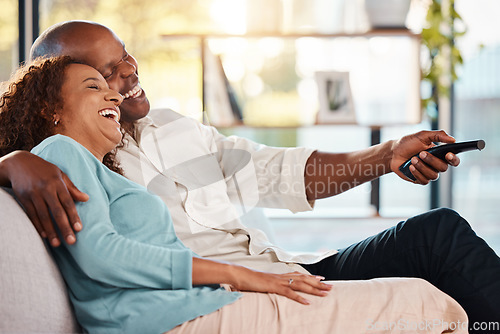 Image of Couple, watching tv and laughing on sofa, hug in home living room and bonding. Interracial, television and funny black man and woman relax on couch streaming comedy movie, comic film or meme video.