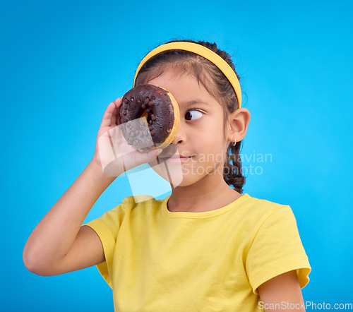 Image of Donut, eye and cover of girl in studio for junk food, sugar and happiness. Snack, cake and cute with face of young child and dessert for eating, sweet and chocolate isolated on blue background