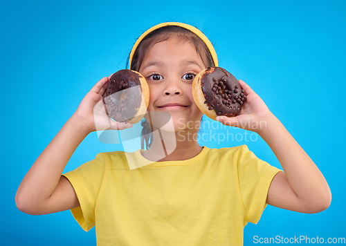 Image of Donut, happy and smile with portrait of girl in studio for junk food, sugar and happiness. Snack, cake and cute with face of child and dessert for eating, diet and chocolate on blue background