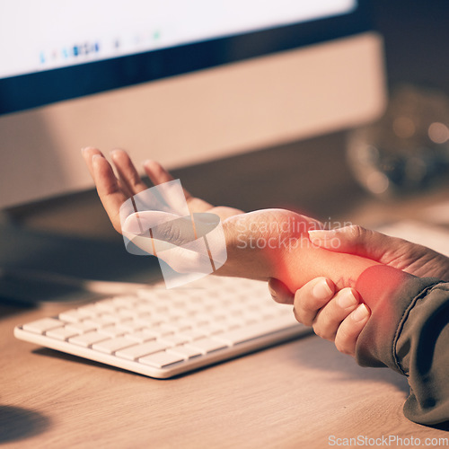 Image of Woman, hands and wrist pain by computer from carpal tunnel syndrome or overworking at night by office desk. Hand of female holding painful arm area or pressure by PC from working late at workplace