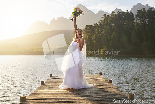 Image of Wedding, bouquet and celebration with a bride on a pier over a lake in nature after a marriage ceremony. Happy, smile and flowers with a woman celebrating being married in the tradition of matrimony