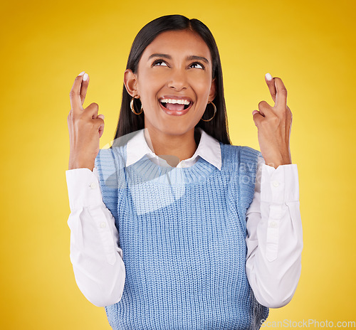 Image of Hope, fingers crossed and young woman in a studio wishing for success, winning or achievement. Happiness, smile and excited Indian female model with a faith hand gesture isolated by yellow background