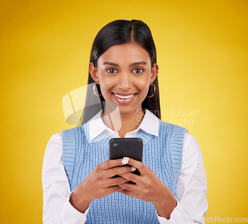 Image of Smile, phone and portrait of woman in studio space typing message or email on yellow background. Technology, communication and happy face of Indian gen z model checking social media or online content