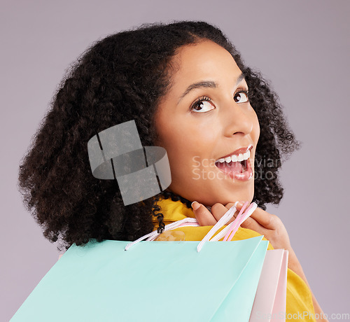 Image of Woman, face and smile with shopping bags for discount, sale or fashion against a gray studio background. Surprised female shopper smiling and holding gifts or shop accessories posing in happiness