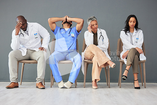 Image of Exhausted, tired and doctors waiting in the hospital with frustration, sad and burnout. Upset, professional and team of healthcare workers sitting in a line in a hallway for meeting in medical clinic