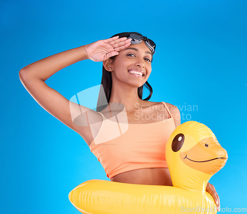 Image of Happy woman, portrait smile and swimming vacation in salute standing with inflatable duck against a blue studio background. Excited female smiling in swimwear ready for swim, pool or travel on mockup