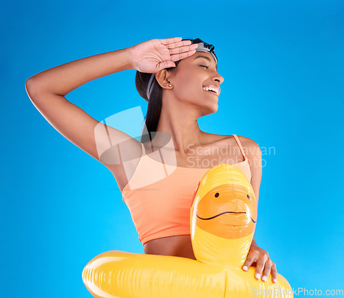 Image of Rubber duck, smile and salute with a swimmer woman in studio on blue background wearing goggles on her head. Happy, hand gesture and swimming with an attractive young female excited to swim in summer