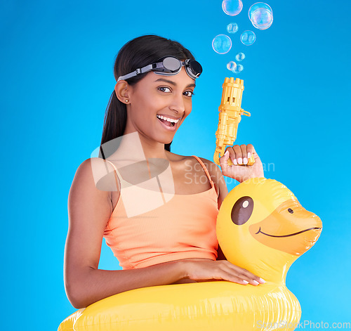 Image of Portrait, bubbles and rubber duck with a woman on a blue background in studio ready for summer swimming. Happy, vacation and goggles with an attractive young female looking excited to relax or swim