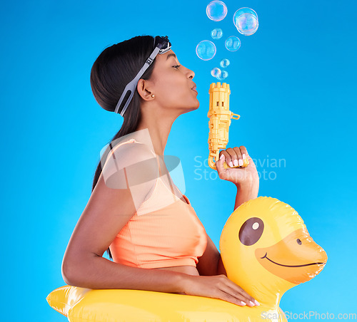 Image of Bubbles, goggles and rubber duck with a woman on a blue background in studio ready for summer swimming. Happy, travel and vacation with an attractive or playful young female blowing a bubble gun