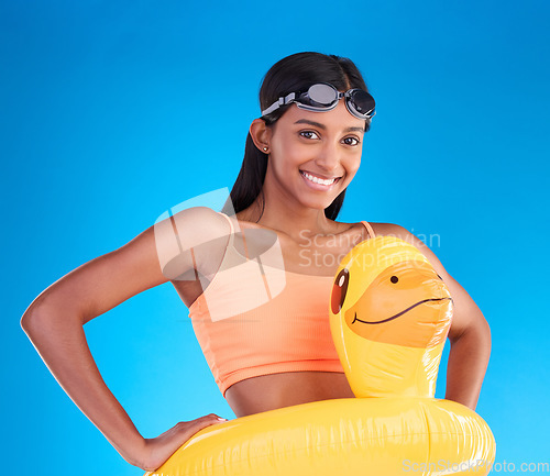 Image of Portrait, goggles and rubber duck with a woman on a blue background in studio ready for summer swimming. Happy, vacation or hands on hips with an attractive young female looking excited for a swim