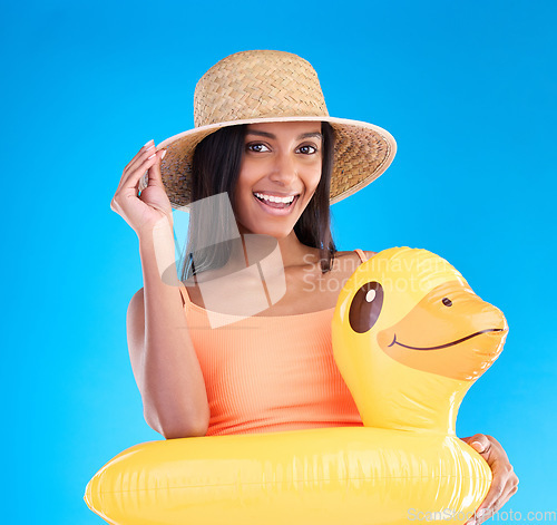 Image of Portrait, hat and rubber duck with a woman on a blue background in studio ready for summer swimming. Happy, travel and vacation with an attractive young female looking excited to relax or swim