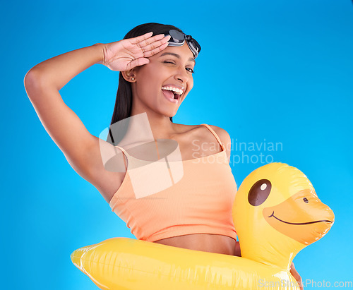 Image of Portrait, smile and salute with a swimmer woman in studio on. a blue background wearing goggles on her head. Happy, hand gesture and swimming with an attractive young female excited to swim in summer