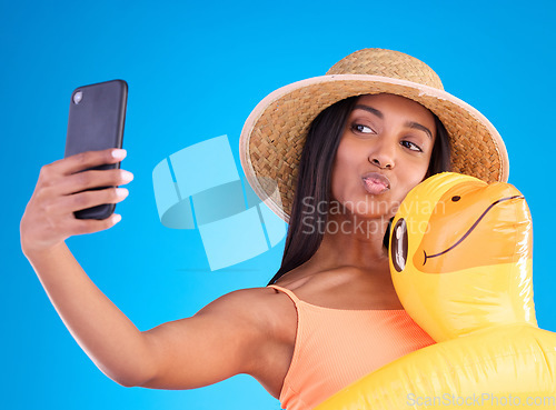 Image of Happy woman, selfie and swimming vacation for social media or profile picture with inflatable duck against a blue studio background. Excited female model in summer swimwear for photo, travel or trip