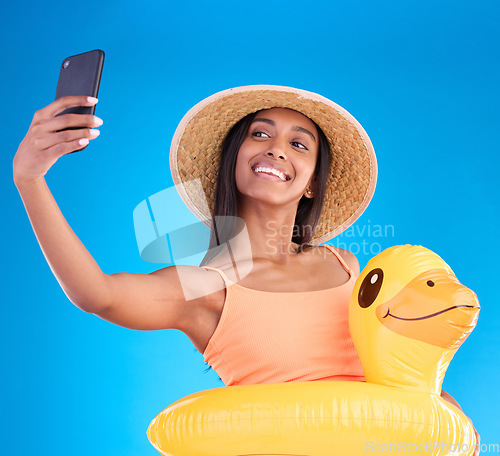 Image of Happy woman, portrait smile and selfie on swimming vacation for profile picture with inflatable duck against a blue studio background. Excited female smiling in swimwear for photo, travel or trip