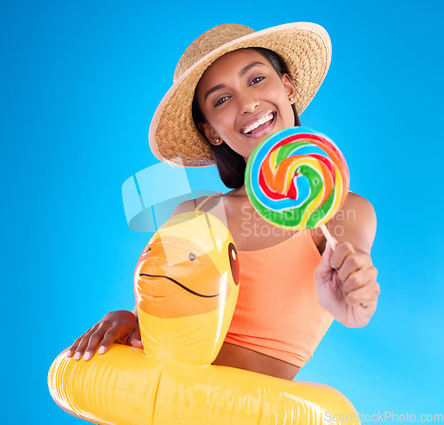 Image of Portrait, lollipop and inflatable duck with a woman on a blue background in studio ready for summer swimming. Happy, travel and vacation with an attractive young female looking excited to relax