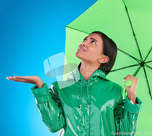 Image of Sad, looking and a woman with an umbrella for the rain isolated on a blue background in a studio. Confused, insurance and a girl waiting for bad weather, disappointed and feeling for water in winter