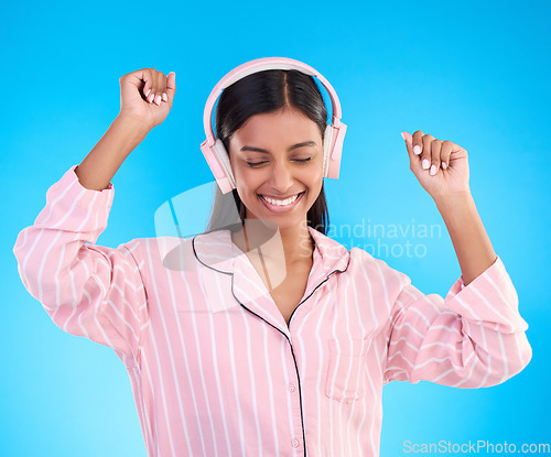 Image of Happy, dance and woman in pajamas, headphones and cheerful on a blue studio background. Female, joyful and lady with headset, waking up and dancing with sounds, streaming music and songs for movement