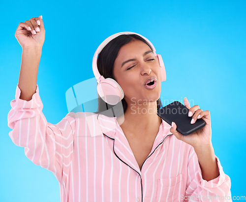 Image of Singing, music and a woman in pyjamas with headphones isolated on a blue background in a studio. Happy, playful and a girl listening to the radio, audio or streaming songs before bedtime on a mobile