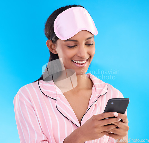 Image of Happy, bedtime and a woman typing on a phone isolated on a blue background in studio. Smile, reading and an Indian girl with social media notification, mobile chat or online communication in pyjamas