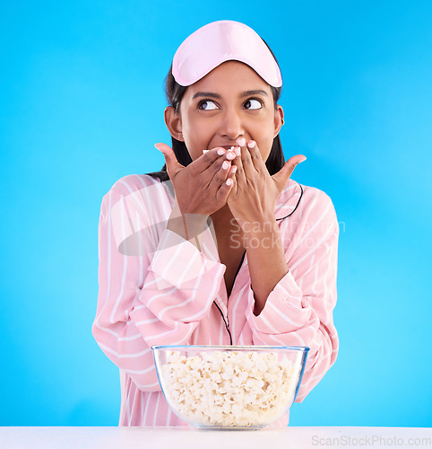 Image of Popcorn, pajamas and thinking with a woman on a blue background in studio watching a movie for entertainment. Idea, video and night with an attractive young female eating a snack while streaming