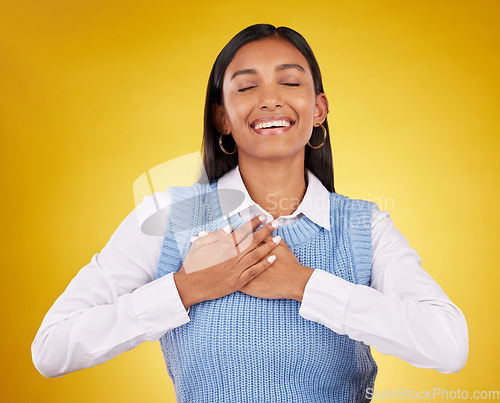 Image of Gratitude, happy and young woman in a studio with her hand on her chest for a grateful expression. Happiness, smile and Indian female model with a thankful hand gesture isolated by yellow background.