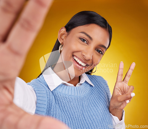 Image of Selfie, peace sign and portrait of Indian woman in studio for happiness, confident and smile on yellow background. Emoji mockup, fashion and girl with hand gesture with beauty, cosmetics and style