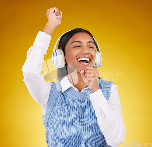 Image of Headphones, energy and female singing in studio while listening to music, playlist or album. Happy, smile and Indian woman model doing karaoke while streaming a song isolated by yellow background.