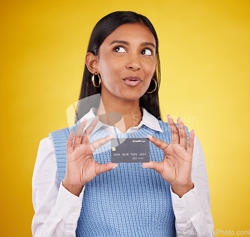 Image of Credit card, thinking and Indian woman on yellow background for bank, investment and payment in studio. Banking mockup, finance and happy girl with plastic for budget, commerce and discount purchase