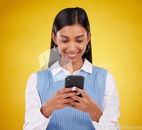 Image of Smile, phone and happy woman in studio typing message, email or web post on yellow background. Technology, communication and happy Indian gen z girl influencer checking social media or online content