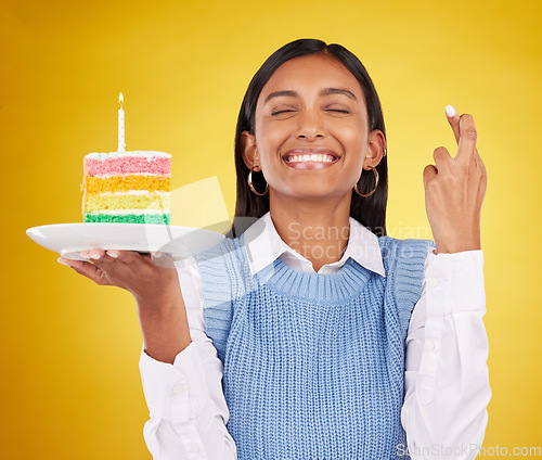 Image of Smile, wish and woman with cake in studio for happy celebration or party on yellow background. Happiness, excited gen z model with fingers crossed and candle in rainbow dessert to celebrate milestone