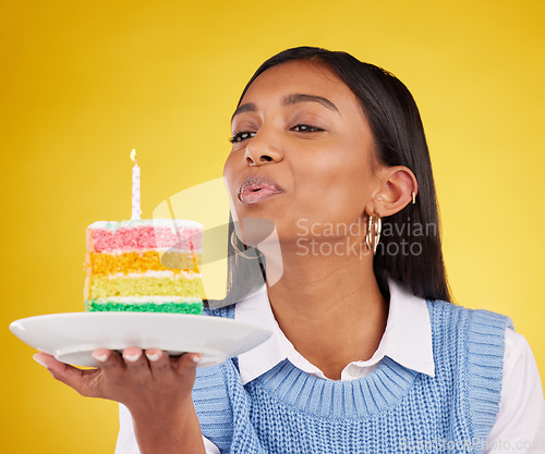 Image of Birthday, cake and woman blowing candle in studio for happy party celebration on yellow background. Happiness, gen z girl and candles in rainbow dessert to celebrate milestone, event or achievement.