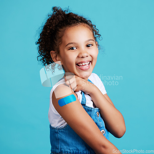 Image of Portrait, smile and girl with plaster, wellness and safety with kid against a blue studio background. Face, young person and female child with happiness, band aid and vaccine with protection and care