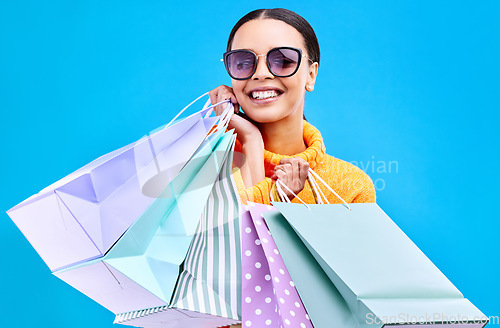 Image of Retail bags, studio and woman portrait with a smile and happiness from boutique sale. Happy, shopping and female model with store bag and sales choice in isolated blue background with sunglasses