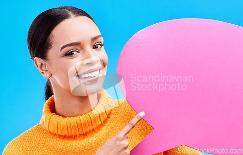 Image of Speech bubble, smile and portrait of woman pointing to banner in studio for advertising on blue background. Face, happy and girl with poster, mockup and space for social media, announcement or news