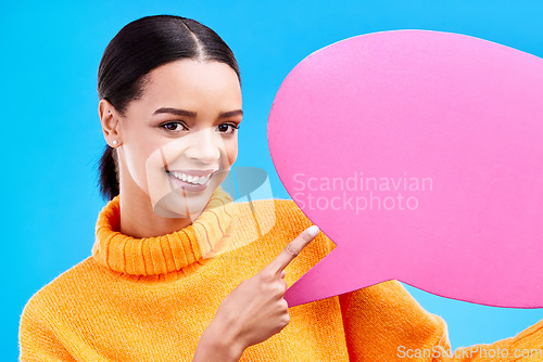 Image of Speech bubble, happy and portrait of woman pointing to banner in studio for advertising on blue background. Face, smile and girl with poster, mockup and space for social media, announcement or news