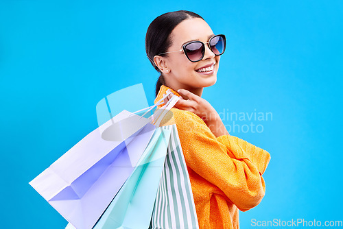 Image of Shopping bags deal, studio and woman portrait with a smile and happiness from boutique sale. Happy, customer and female model with store bag and sales in isolated blue background with sunglasses