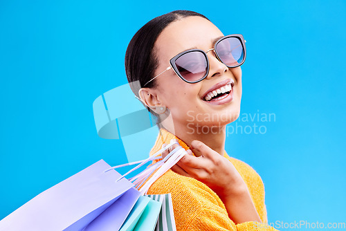 Image of Shopping bags, retail and woman portrait with a smile and sunglasses from boutique sale. Happy, customer and female model with store bag and sales choice in isolated blue background in studio