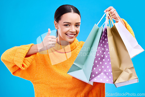 Image of Happy woman, shopping bags and thumbs up for purchase, sale or discount against a blue studio background. Portrait of female shopper holding gift bag showing thumb emoji, yes sign or like for items