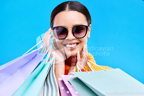 Image of Shopping bags, studio and happy woman portrait with a smile and happiness from boutique sale. Sunglasses, customer and female model with store bag and sales choice in isolated blue background