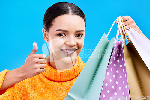 Image of Happy woman, portrait smile and shopping bags with thumbs up for purchase, sale or discount against blue studio background. Face of female shopper with gift bag showing thumb emoji, yes sign or like