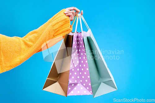 Image of Woman, hands and shopping bags in studio of purchase, luxury accessories or sale against a blue background. Hand of female shopper holding gift bag, buy or presents of retail products on mockup