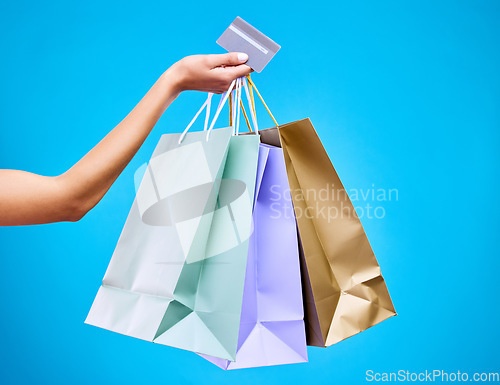 Image of Woman, hands and shopping bags with credit card for purchase, sale or discount against a blue studio background. Hand of female shopper holding gift bag or presents for banking transaction or buying