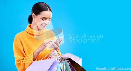 Image of Happy woman, phone and shopping bags on mockup for purchase, sale or discount against a blue studio background. Excited female shopper smiling on mobile smartphone holding gift bag on copy space