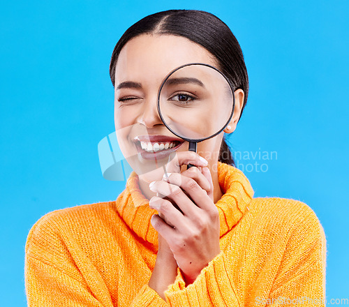 Image of Happy, portrait and woman with a magnifier in a studio for an investigation or detective cosplay. Happiness, smile and headshot of a female model with a magnifying glass isolated by a blue background