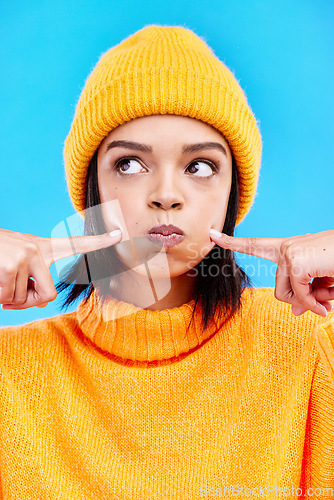 Image of Silly, goofy and young woman in a studio with a comic, funny and crazy face expression. Funny, humor and beautiful female model from Puerto Rico touching her cheeks isolated by a blue background.