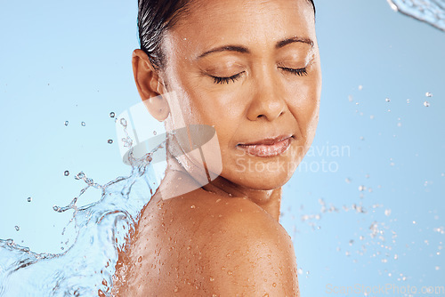 Image of Water splash, skincare and woman on blue studio background health, wellness and hygiene with cleaning routine. Shower, cosmetic beauty and relax, mature model in skin care or dermatology treatment.