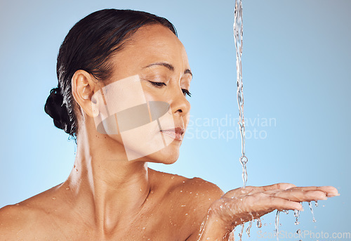 Image of Mature, grooming and a woman catching water for beauty isolated on a blue background in a studio. Skincare, hygiene and a model in the shower for morning routine, body care and washing on a backdrop