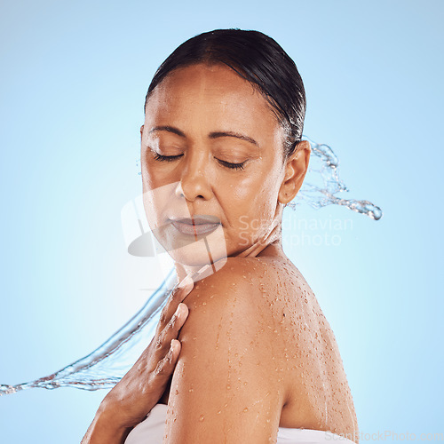 Image of Skincare, shower and a mature woman with a water splash isolated on a blue background in a studio. Glow, anti aging and a model with hydration, liquid and fluid for skin, grooming and hygiene